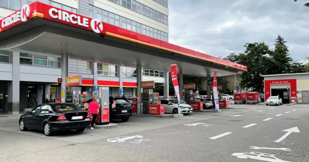 Stacja paliw Circle K z dystrybutorami, samochodami i budynkiem myjni.