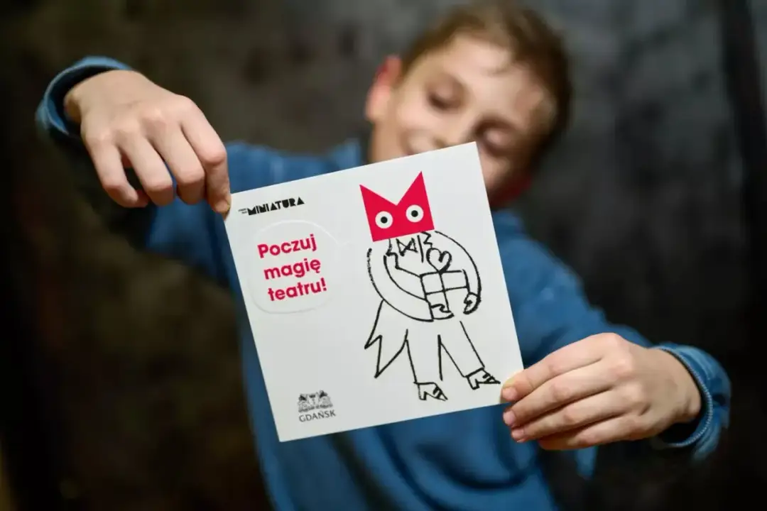 Chłopiec trzyma kartkę z napisem "Poczuj magię teatru!". To zaproszenie na spektakl, idealne bilety do teatru dla dzieci.