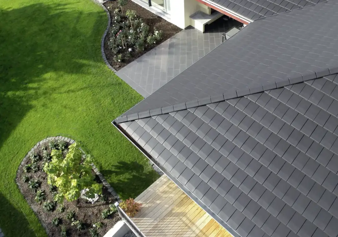 Nowoczesne, ciemnoszare płyty na dach idealnie komponują się z zielonym ogrodem i drewnianym tarasem, tworząc harmonijną całość.