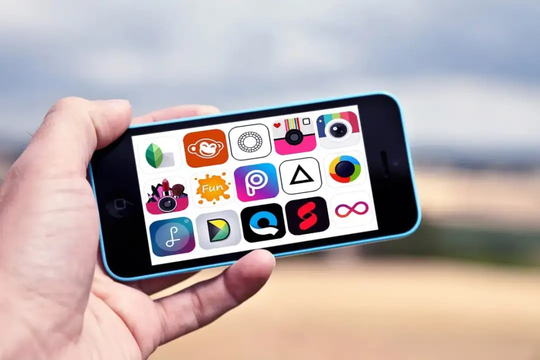 Dłoń trzyma smartfon z widokiem na ekranie wielu ikon aplikacji do edycji zdjęć.