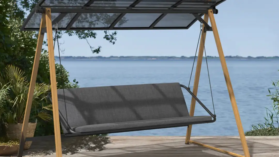 Huśtawka ogrodowa z drewnianą ramą i szarym siedziskiem, na tle wody.
