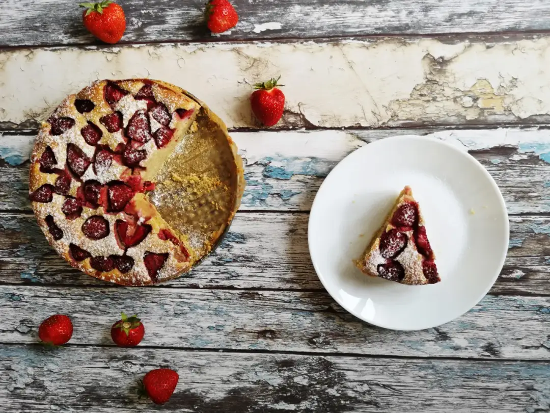 Ciasto z truskawkami, posypane cukrem pudrem, obok talerzyk z kawałkiem. Czy mąka owsiana nadaje się do ciasta? Wygląda na to, że tak!