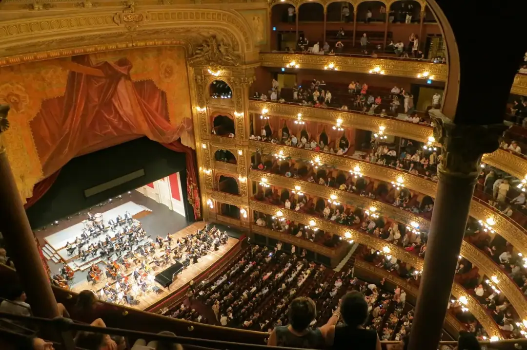 Widok z góry na salę teatralną z orkiestrą na scenie i publicznością na widowni.