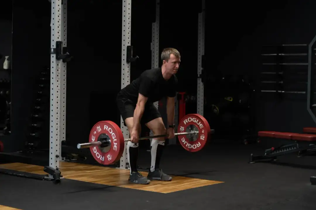Mężczyzna w czarnym stroju przygotowuje się do martwego ciągu. Ćwiczenie to buduje siłę całego ciała.