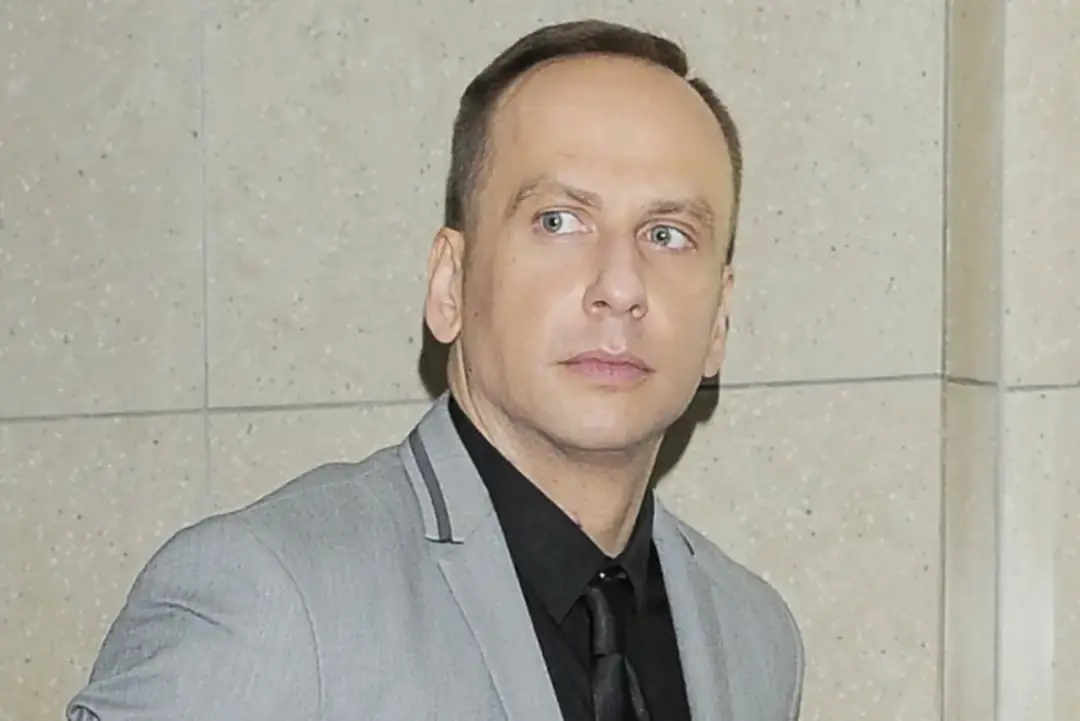 Dariusz Krupa obecnie, w szarym garniturze i czarnej koszuli, spogląda w bok.