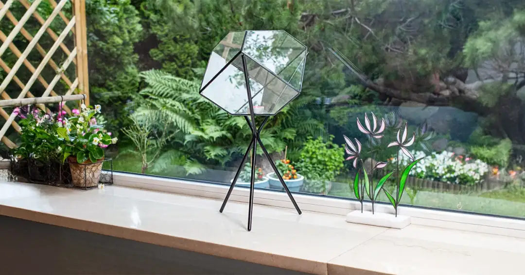 Parapet z kwiatami w doniczkach, szklanym lampionem i witrażem kwiatowym.