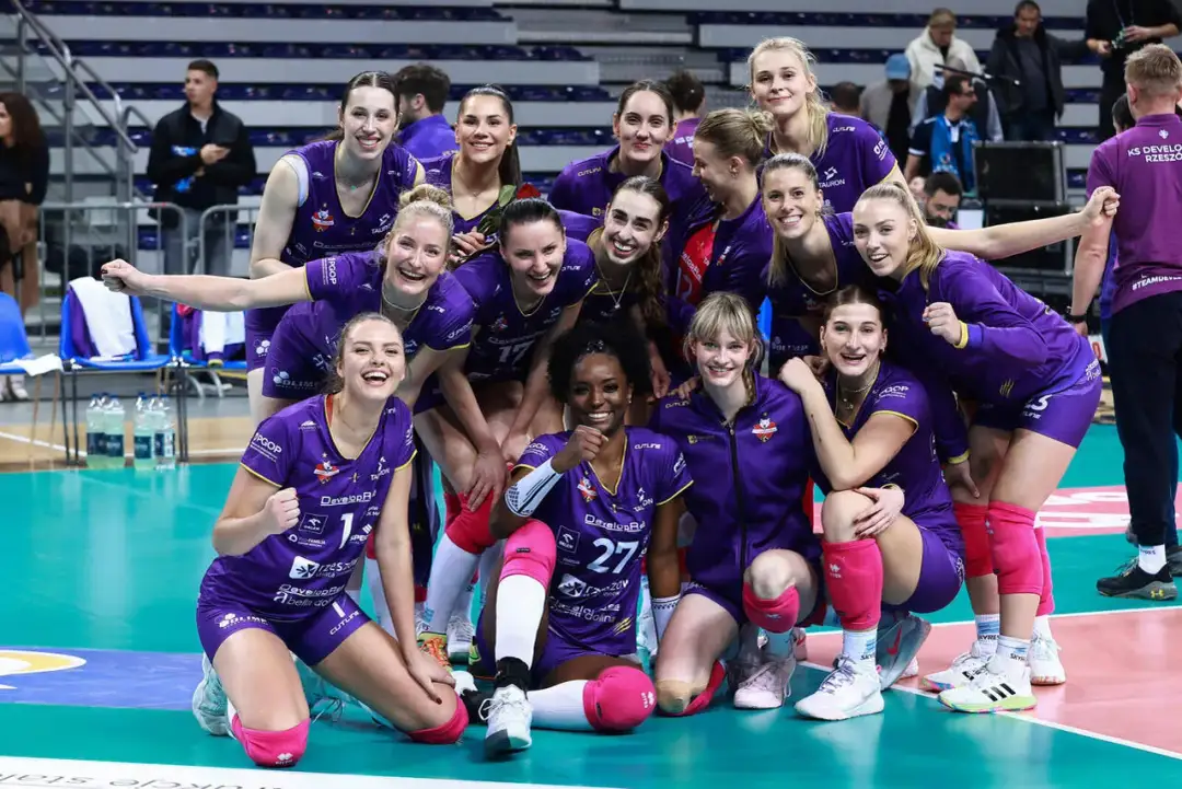 Uśmiechnięte siatkarki Savino Del Bene Scandicci w fioletowych strojach świętują zwycięstwo.
