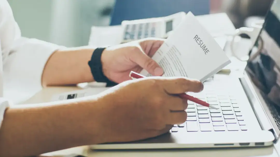 Osoba przegląda CV na laptopie, zastanawiając się, czy kłamstwo w CV lub naciąganie doświadczenia zawodowego się opłaca.