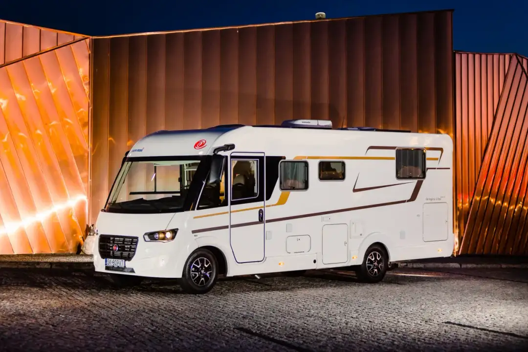 Biały kamper Integra Line na tle nowoczesnej, oświetlonej ściany. Zastanawiasz się, ile kosztuje kamper?