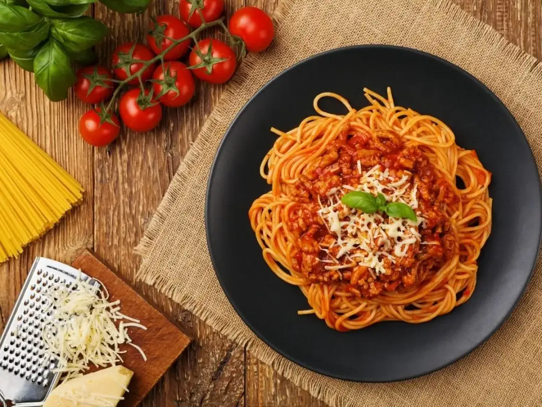 Pyszne spaghetti bolognese na talerzu, z pomidorami i bazylią. Idealne, by dowiedzieć się, jak pasteryzować sos do spaghetti z mięsem mielonym.