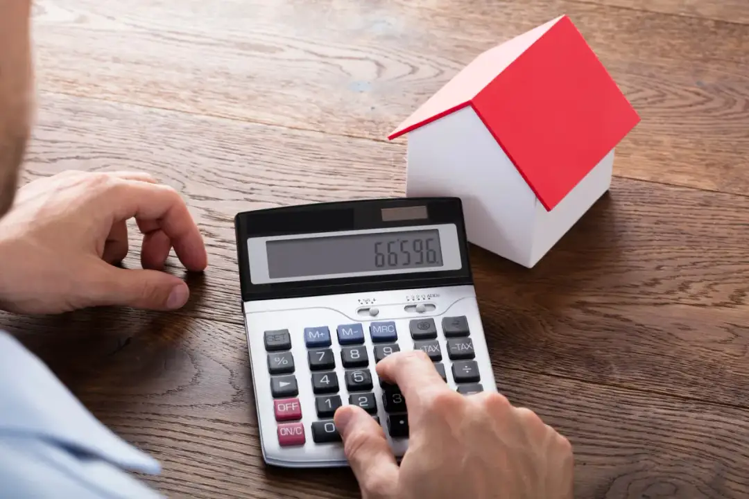 Obliczanie podatku od nieruchomości. Czy podatek od nieruchomości płaci każdy właściciel? Kalkulator i model domu na drewnianym stole.