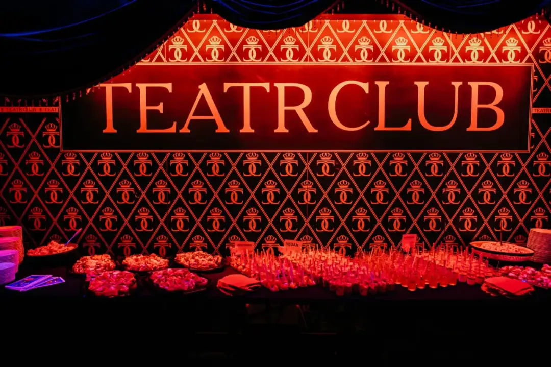 Elegancka ściana z napisem TEATR CLUB i wzorem koron. Na pierwszym planie stół z przekąskami i kieliszkami.