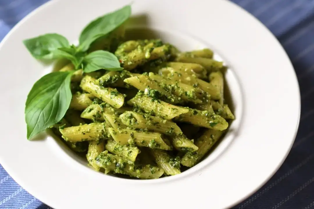 Penne z aromatycznym pesto i kawałkami pomidorów, udekorowane świeżą bazylią. Pyszne danie, które zachwyca smakiem.