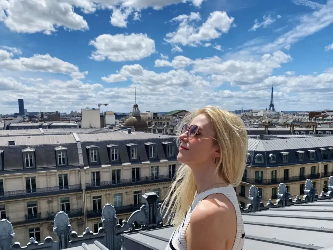 Kobieta na tarasie widokowym Galerii Lafayette podziwia panoramę Paryża z Wieżą Eiffla w tle.