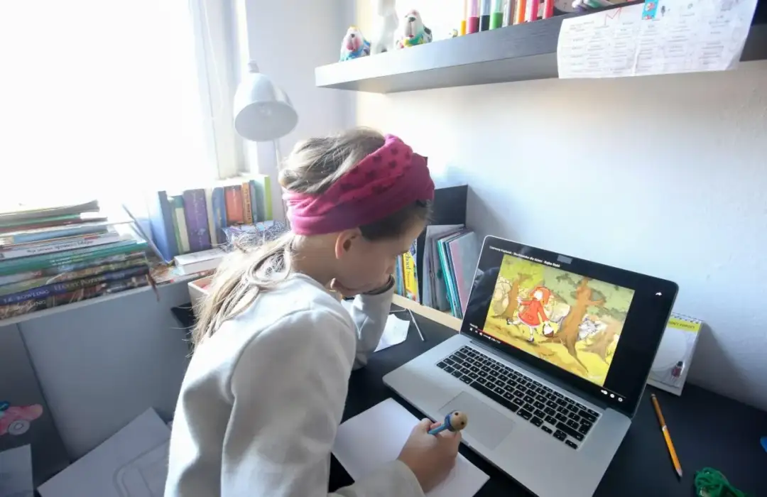 Dziewczynka z opaską na głowie uczy się zdalnie, oglądając bajkę na laptopie.