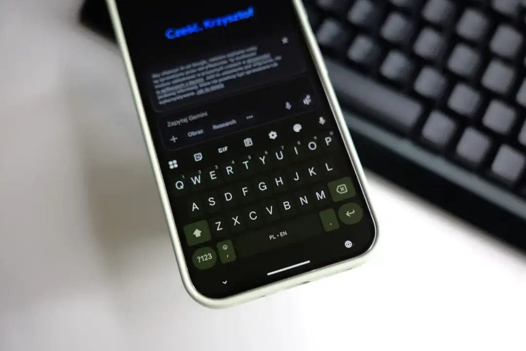 Klawiatura Gboard na telefonie wyświetla zapytanie do Gemini. Widoczny jest też fragment klawiatury fizycznej.