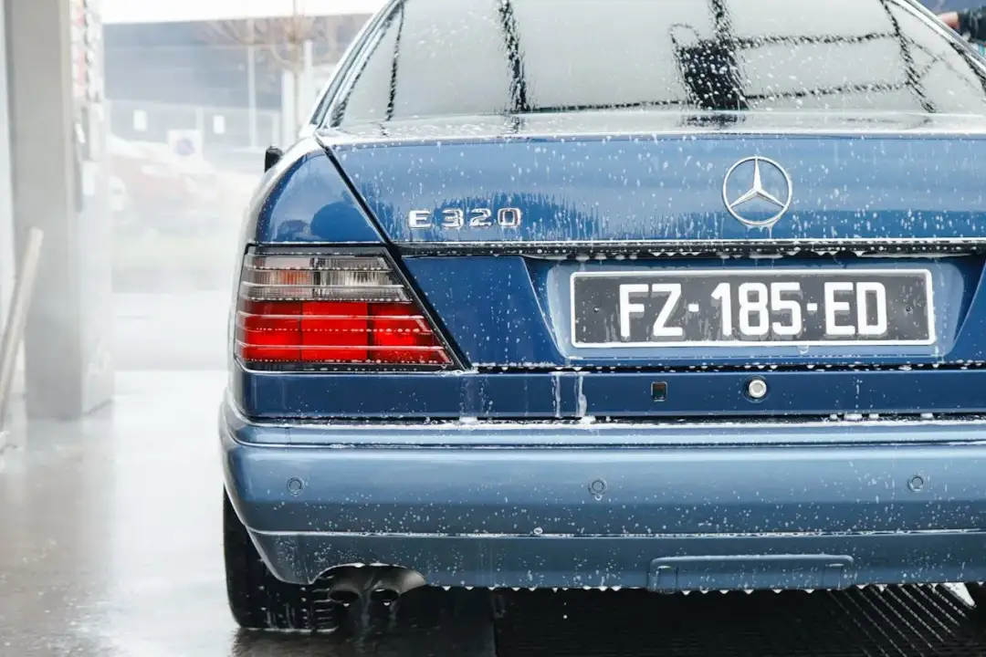 Niebieski Mercedes E320 na myjni, pokryty pianą. Pokazane tylne światła i tablica rejestracyjna FZ-185-ED. To dobry przykład, jak myć auto na myjni.