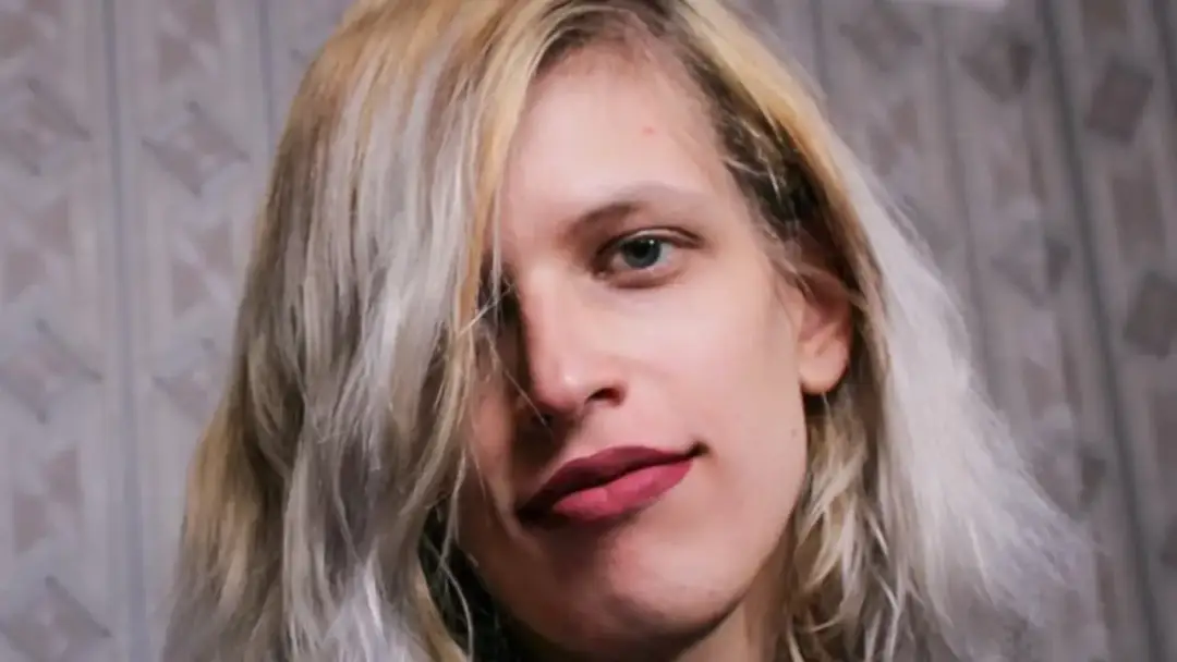 Portret młodej kobiety z blond włosami i niebieskimi oczami. Jej usta są pomalowane na ciemny róż. To pytanie, co to znaczy cis kobieta, jest często zadawane.