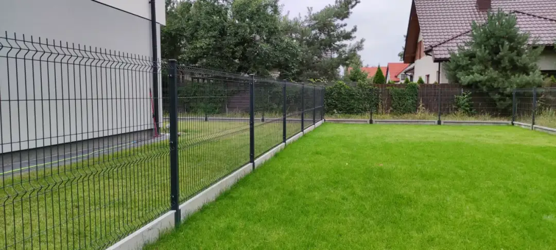 Ogrodzenie panelowe z podmurówką betonową na tle domu i zielonego trawnika.