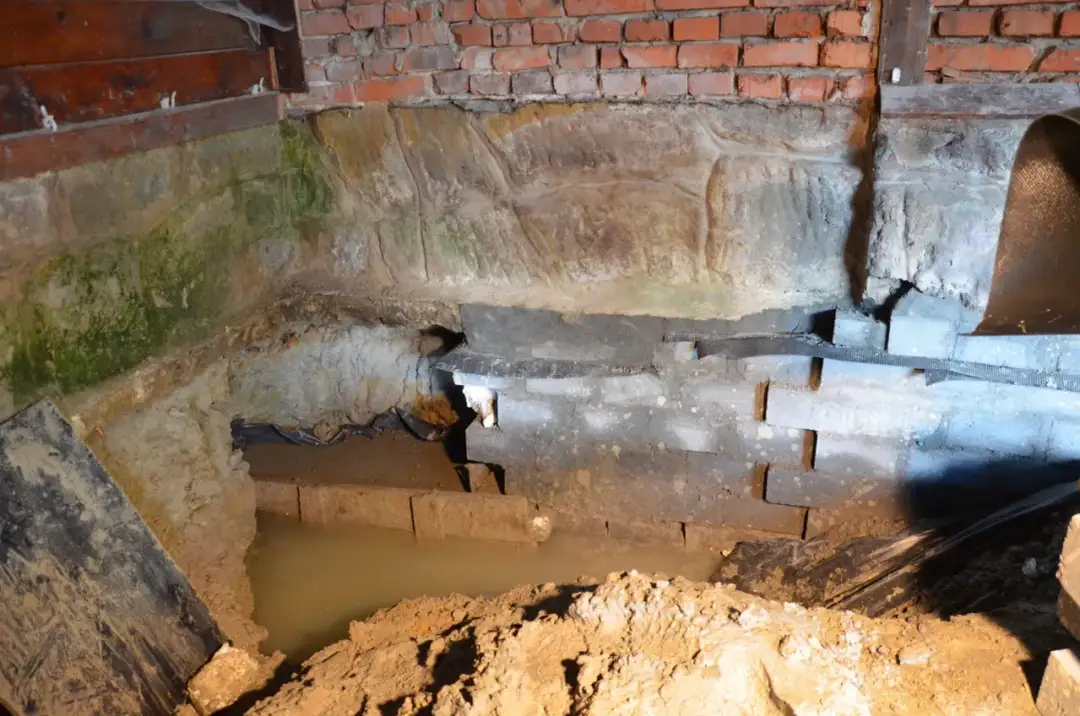 Prace przy hydroizolacji fundamentów od wewnątrz. Widoczny wykop, wilgoć i elementy konstrukcyjne.