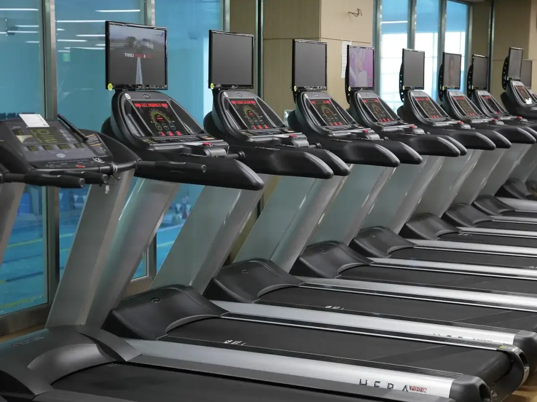 Rząd bieżni magnetycznych z ekranami w siłowni.