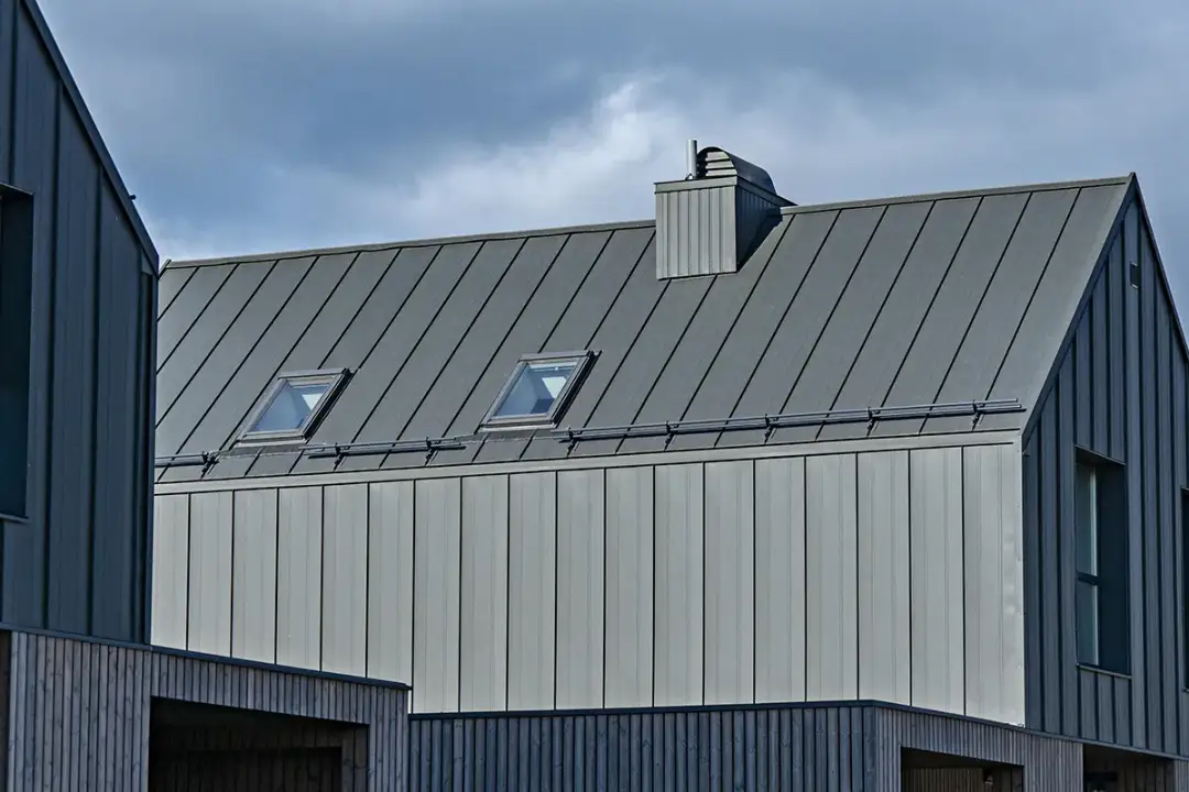 Nowoczesna elewacja z blachy na rąbek, z dwoma oknami dachowymi i kominem.