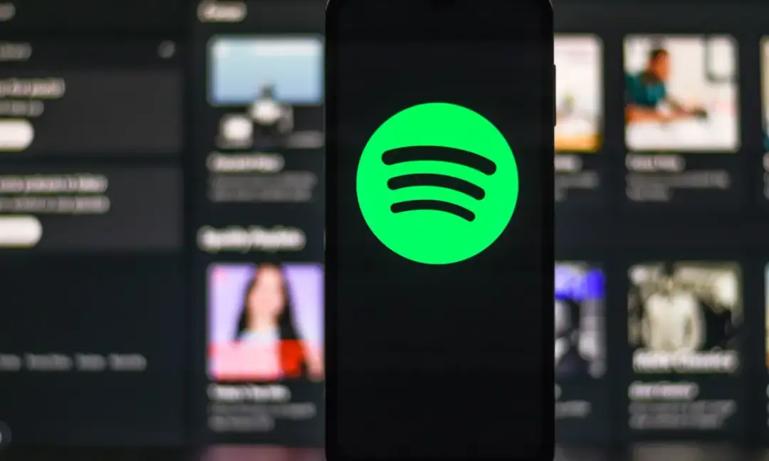 Telefon z logo Spotify na ekranie, w tle widoczne inne playlisty.