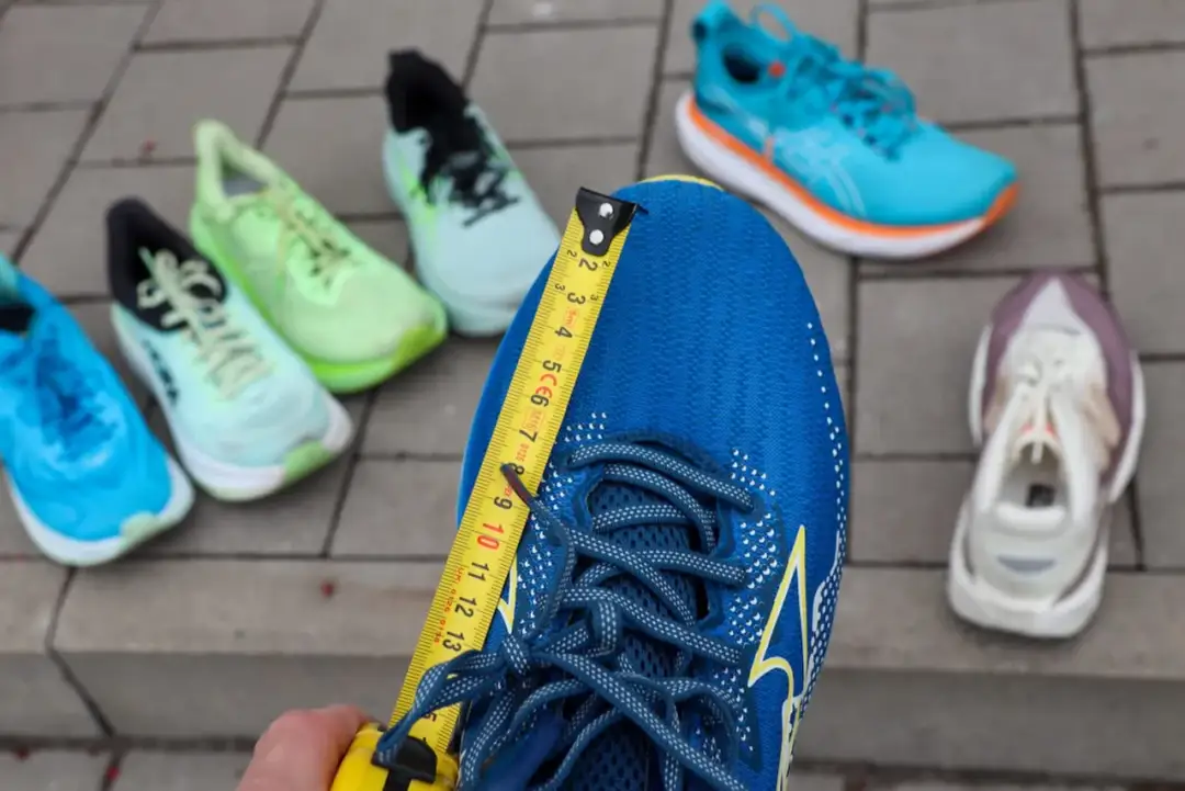 Miarka mierzy niebieski but do biegania. Czy buty do biegania powinny być większe? W tle inne kolorowe buty.