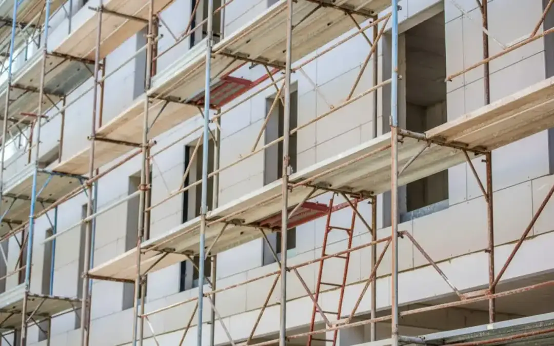 Rusztowanie wokół budynku, z drewnianymi platformami i metalowymi elementami. Pomaga to zrozumieć, jak obliczyć ilość rusztowania potrzebną do budowy.