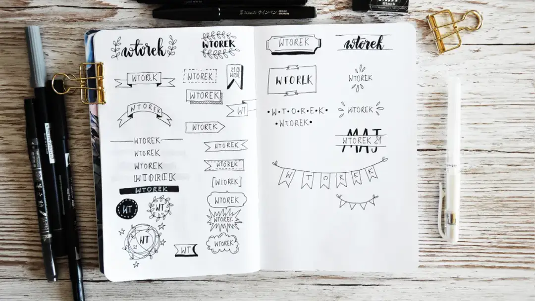 Otwarty notatnik z różnymi stylami napisów "WTOREK" i ozdobnymi elementami.