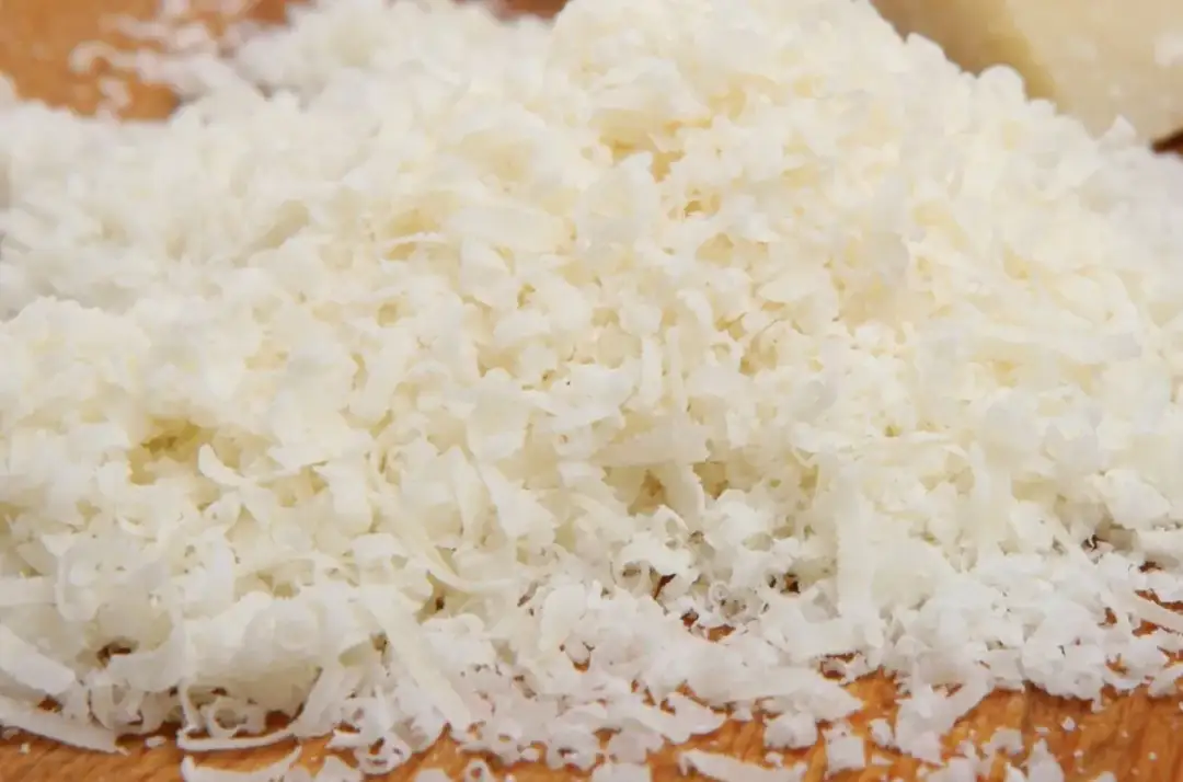 Stos tartych kawałków parmezanu na drewnianej desce.