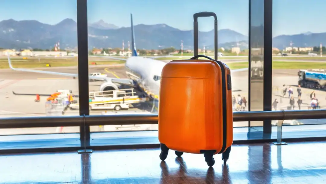 Pomarańczowa walizka czeka na lotnisku. Zastanawiasz się, ile może ważyć bagaż podręczny, by zmieścić się w limitach?