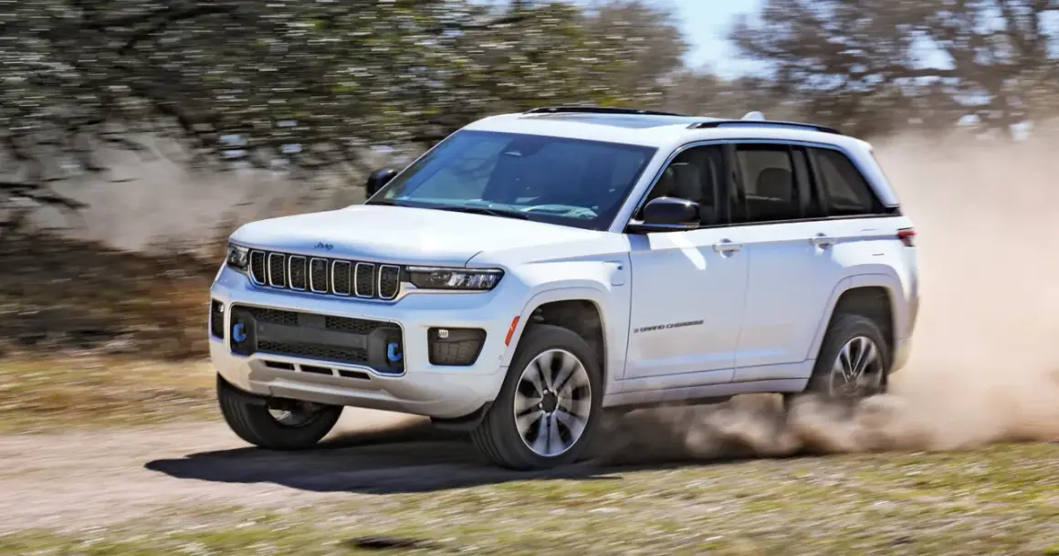 Biały Jeep Grand Cherokee z napędem 4x4 pokonuje piaszczystą drogę, wzbijając tumany kurzu.