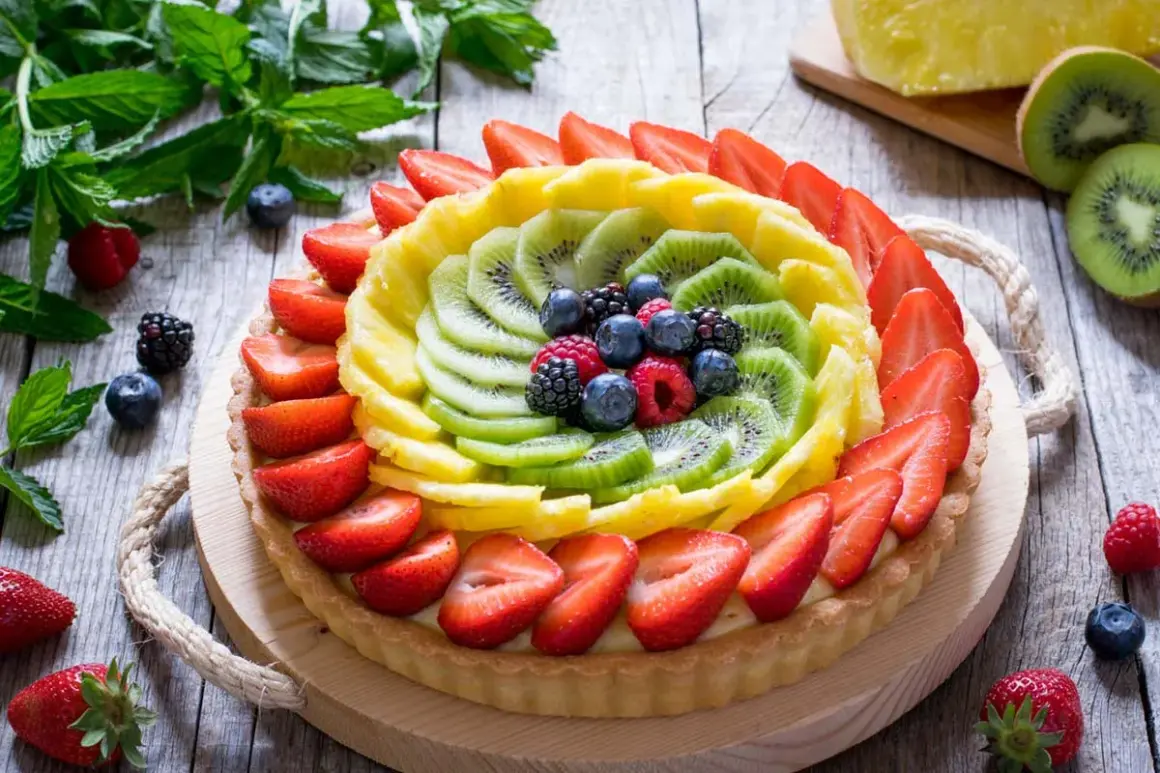 Crostata di frutta con decorazioni colorate di fragole, kiwi, ananas e frutti di bosco.
