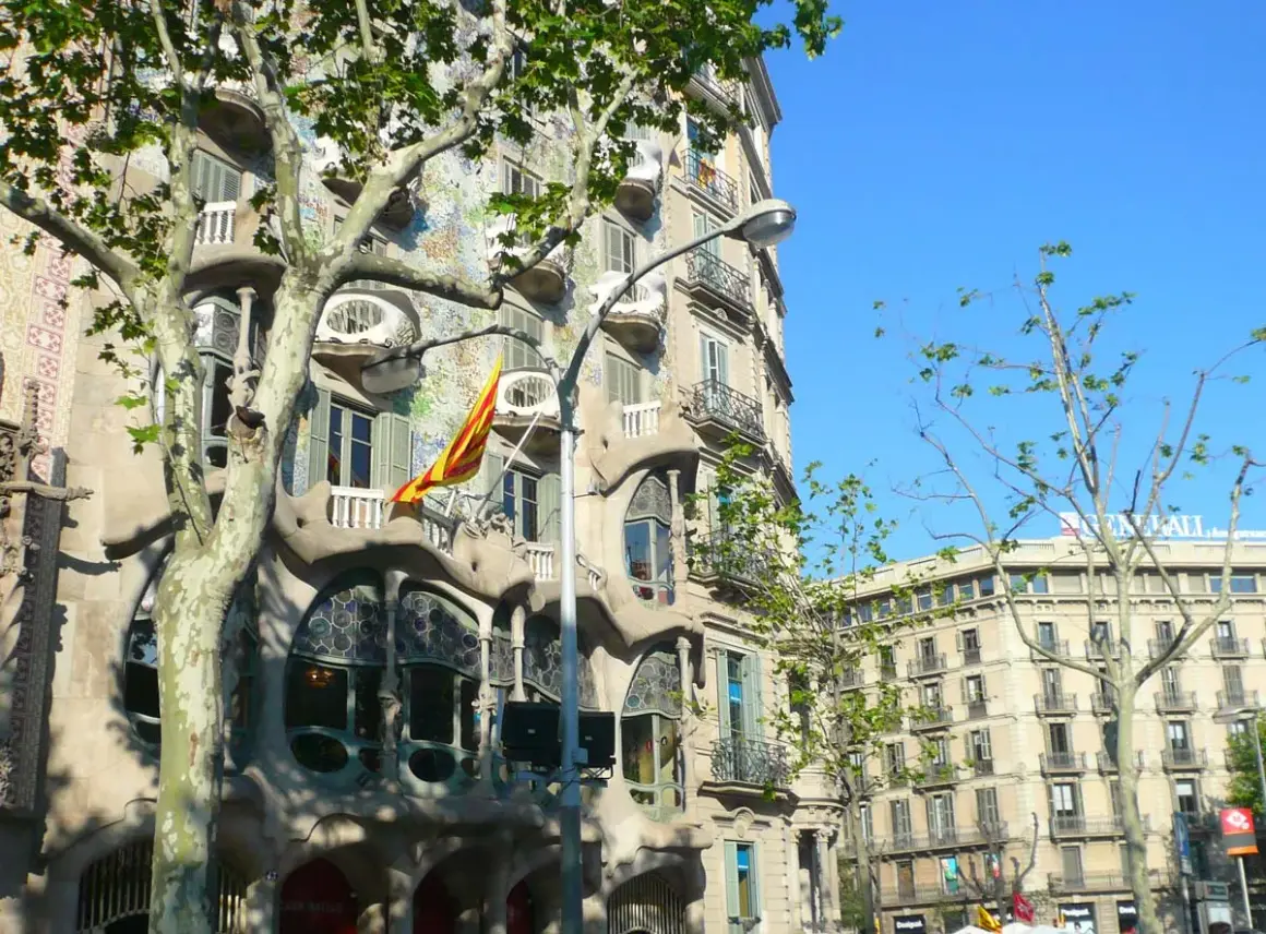 La Casa Batlló, joya modernista, luce su fachada ondulante y colorida bajo el sol. Una bandera catalana ondea, celebrando Sant Jordi.