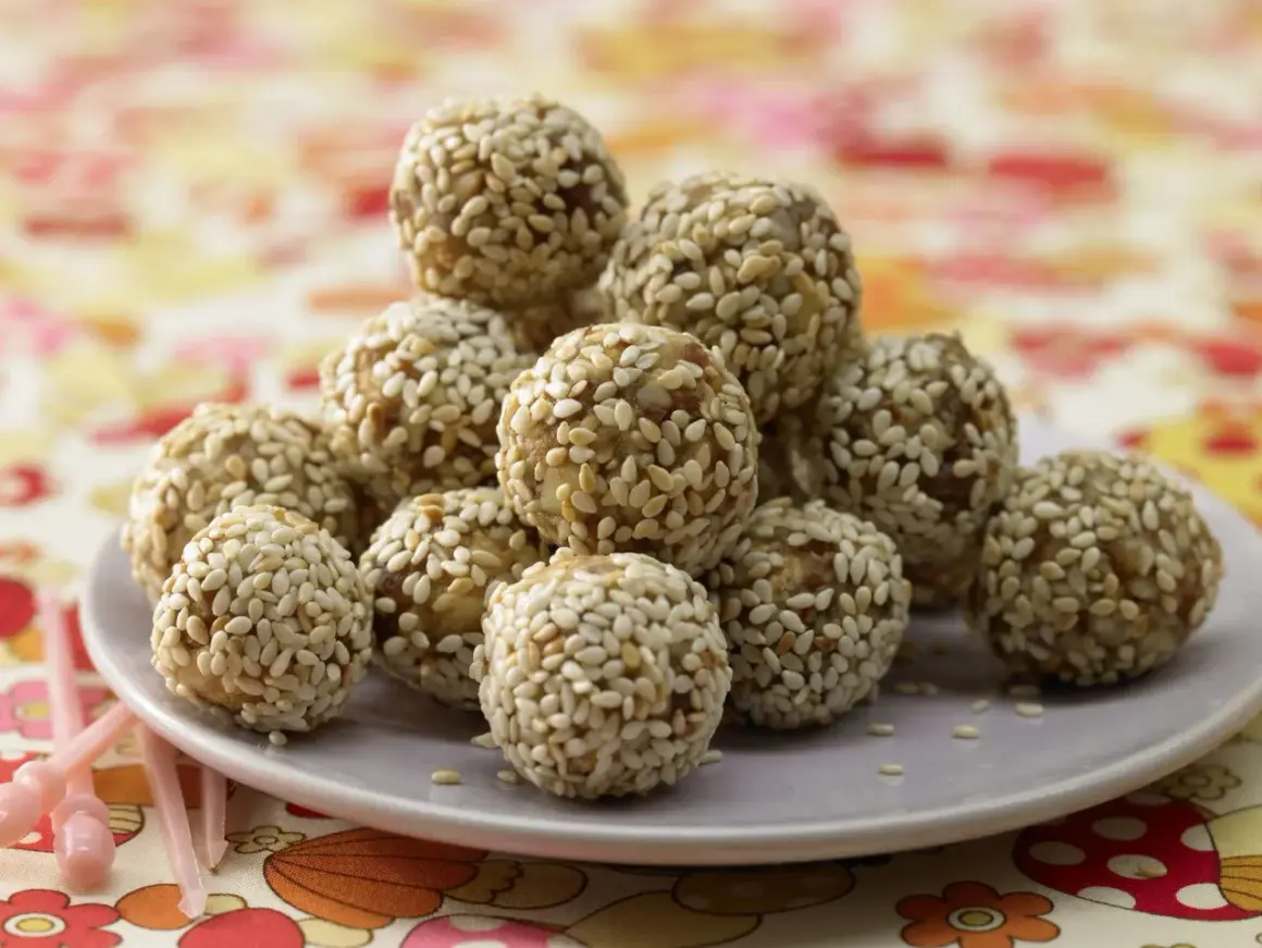 Ein Haufen köstlicher Energy Balls, umhüllt von Sesam, auf einem Teller. Perfekt für einen schnellen Energieschub!