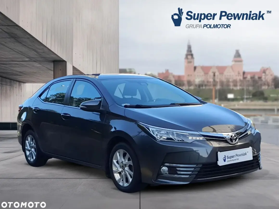 Szary sedan Toyota Corolla używane z salonu, z logo "Super Pewniak" na tablicy rejestracyjnej.