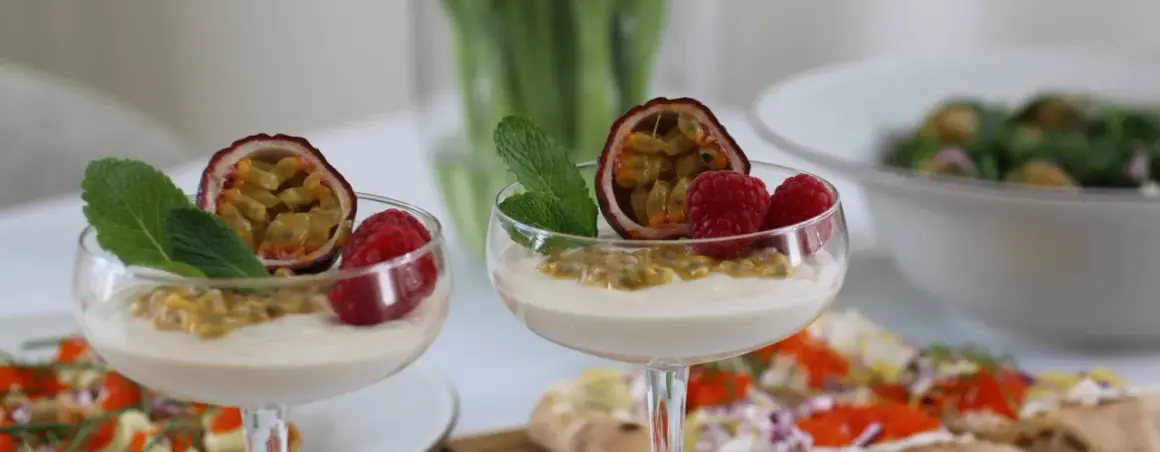 Två glas med len vit chokladmousse, toppade med passionsfrukt, hallon och mynta. En läcker dessert som passar perfekt till fikat.