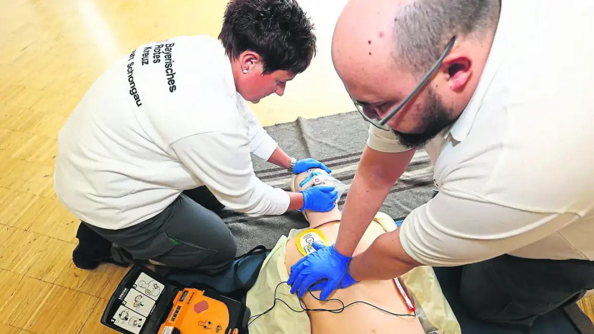 Zwei Personen üben die Defibrillator Anwendung an einer Puppe. Ein Mann führt Herzdruckmassage durch, während eine Frau die Beatmungsmaske hält.