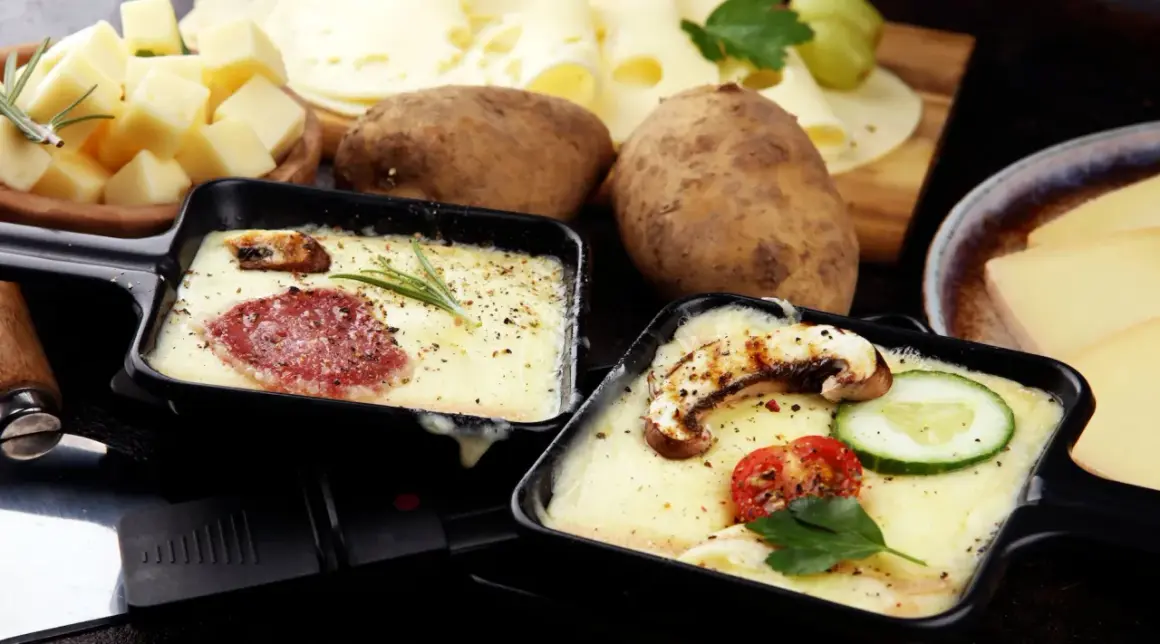 Schmelzender Raclette-Käse mit Salami und Pilzen, dazu Kartoffeln und ein Glas Wein. Perfekt für einen gemütlichen Abend.