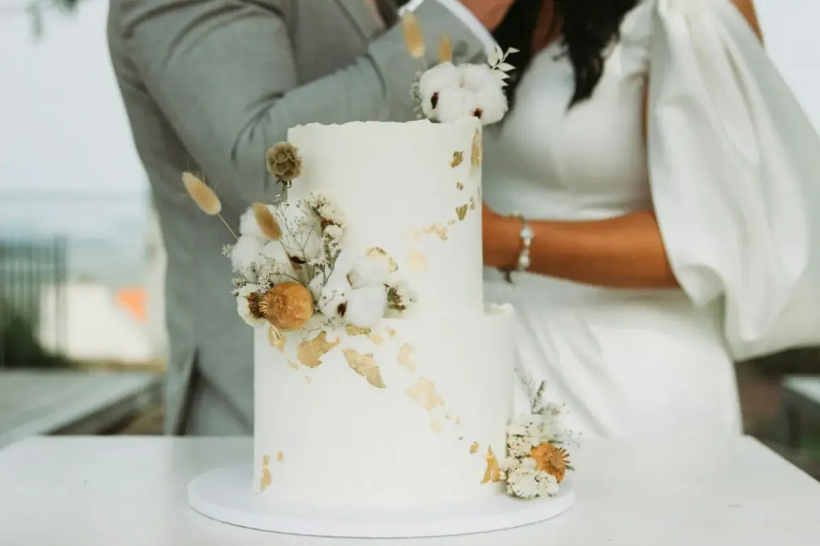 Torta nuziale bianca decorata con fiori secchi e dettagli dorati, perfetta per le canzoni per taglio torta.