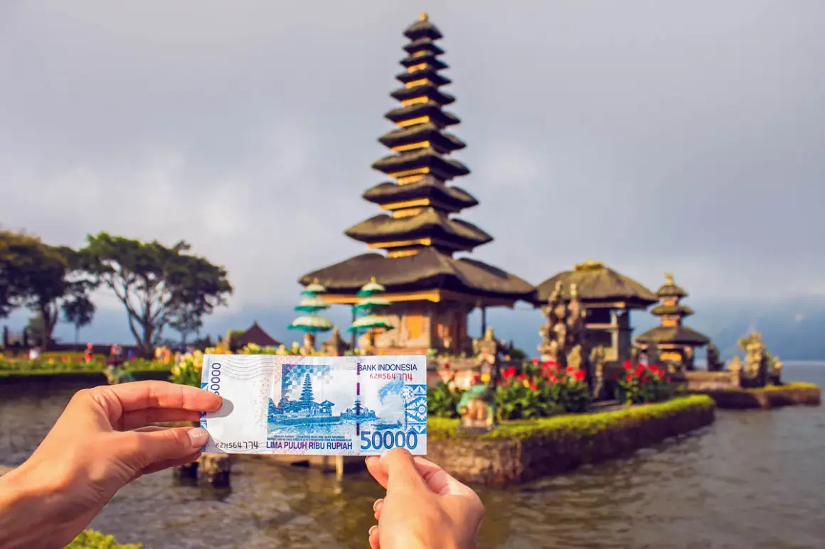 Ręka trzyma banknot 50 000 rupii indonezyjskich na tle świątyni na wodzie na Bali.