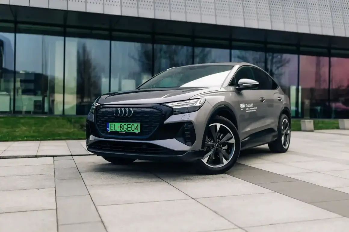 Szary Audi Q4 elektryk z zieloną tablicą rejestracyjną stoi przed nowoczesnym budynkiem.