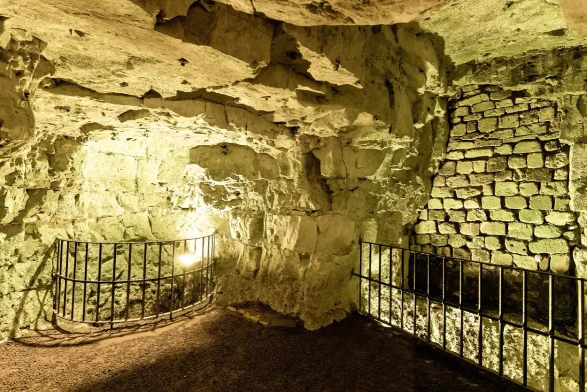 Intérieur des boves d'Arras, un réseau de galeries souterraines aux murs de pierre brute et de briques, éclairées par une lumière jaune.