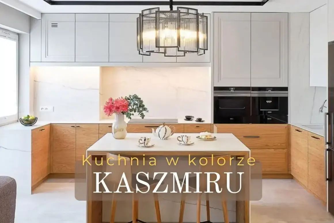 Elegancka kuchnia w kolorze kaszmiru z drewnianymi frontami i marmurowym tłem. Na wyspie bukiet kwiatów i zastawa.