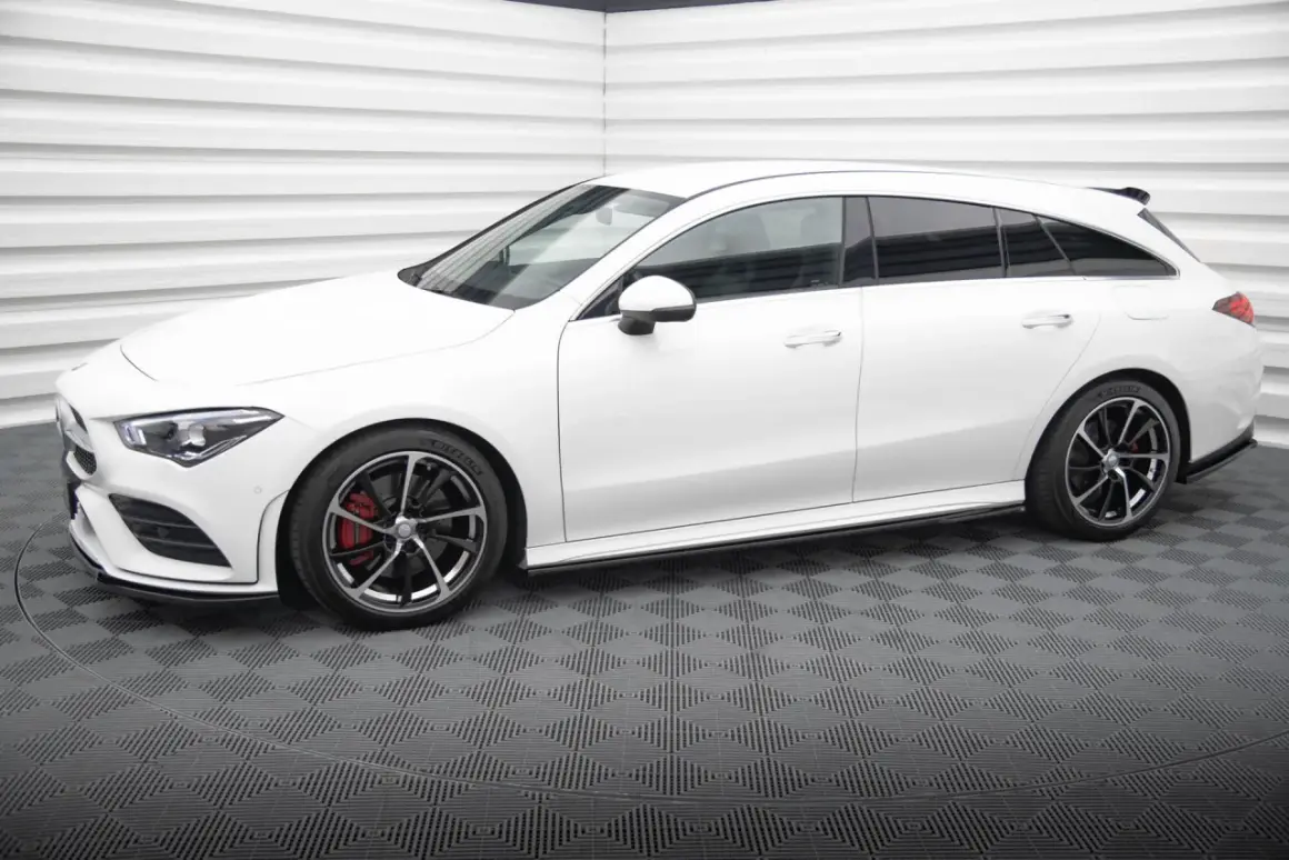 Biały Mercedes CLA shooting brake z czarnymi felgami i czerwonymi zaciskami hamulcowymi stoi na szarej, kratkowanej podłodze.
