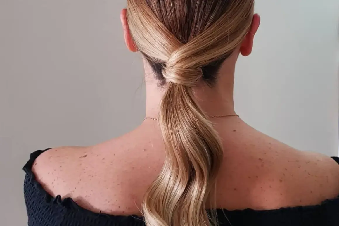 Capelli biondi raccolti in una coda bassa con un'elegante torsione, perfetta per una cerimonia.