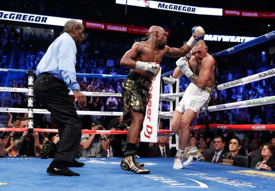 A referee watches as Floyd Mayweather Jr. lands a punch on Conor McGregor during their boxing match.