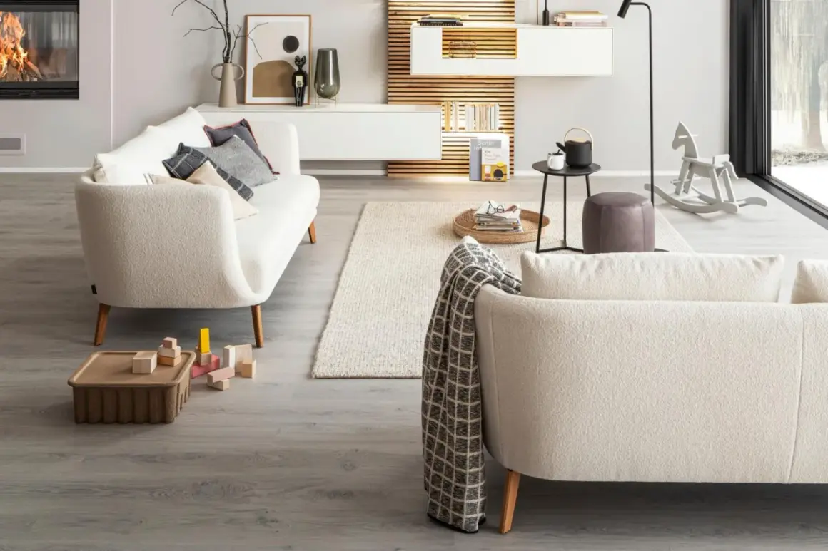 Gemütliches Wohnzimmer mit einem cremefarbenen Sofa vor bodentiefen Fenstern. Ein Kaminfeuer wärmt den Raum.