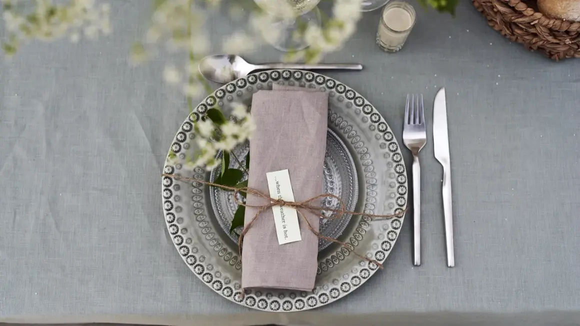 Vackert dukat bord med en lila servett vikt som en blomma, knuten med snöre. En liten lapp med texten "...when the weather is hot" sitter fäst.